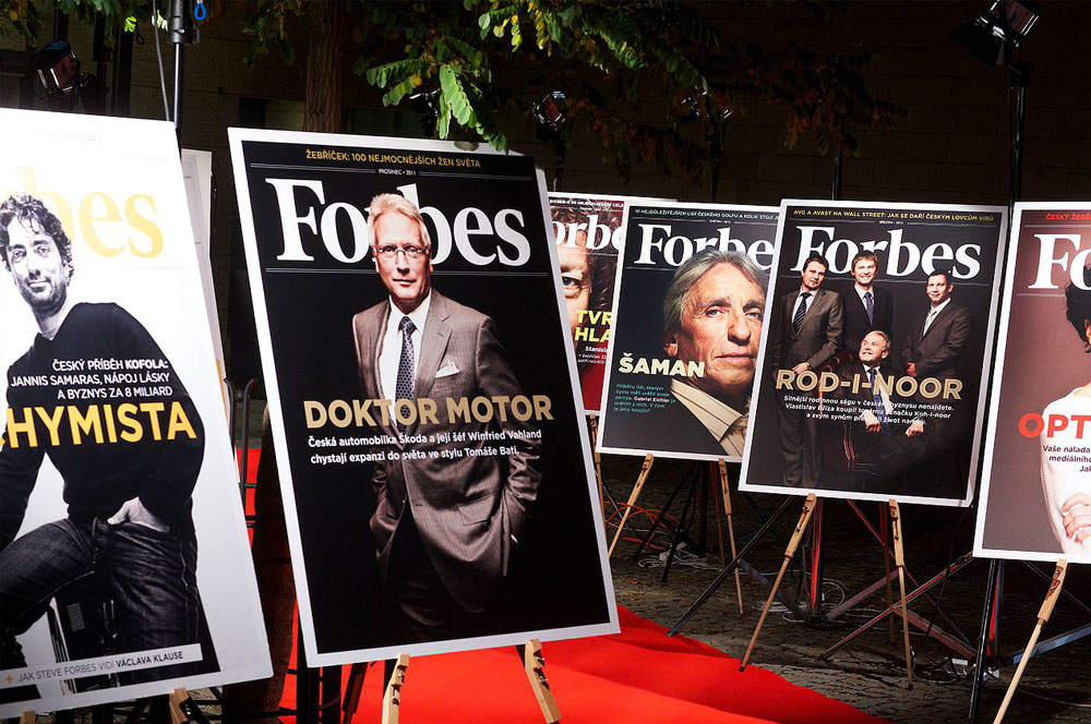 Zvětšené titulní strany magazínu Forbes na stojanech podél červeného koberce